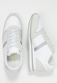 Baskets blanches avec des accents en daim gris doux, un design lisse, une fermeture à lacets en tissu et une bande argentée. Semelle texturée pour une meilleure adhérence.