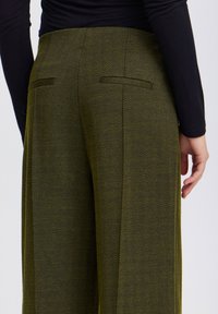Hlače s naivo houndstooth v olivno zeleni barvi in prilagojenim krojem, z dvema zadnjima žepoma in gladkim teksturiranim materialom.