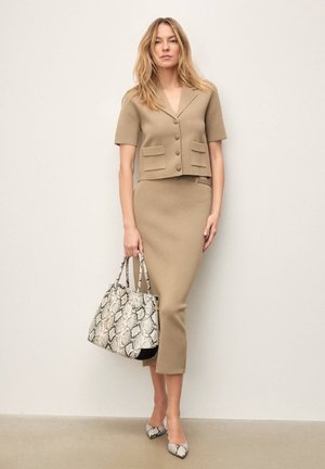 Bézs kötött két részes szett, rövid ujjú, zsebes, rövidített blézerrel és alakra szabott szoknyával, kígyóbőr mintás táskával és hozzá illő magas sarkú cipővel párosítva.