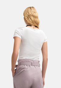 Biała koszulka z krótkim rękawem i okrągłym dekoltem, w zestawieniu z jasnofioletowymi spodniami o wysokim stanie, z szerokim paskiem i bocznymi kieszeniami.