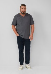 Szary t-shirt z dekoltem w serek wykonany z miękkiego materiału, zestawiony z ciemnoniebieskimi dżinsami i białymi trampkami. Luźny krój, krótkie rękawy i minimalistyczny design.