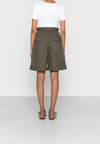 Olivengrønne shorts med elastisk talje, sidelommer og opskåret kant, parret med en tætsiddende hvid T-shirt og flade sandaler.