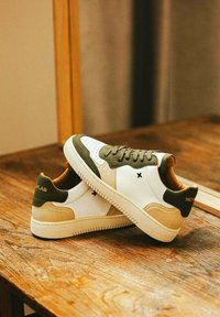 Baskets blanches en cuir avec des accents verts, des détails en suède beige et un intérieur tan. Caractéristiques : design à lacets et semelle en caoutchouc texturée.
