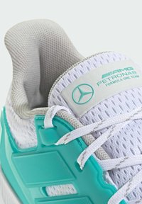 Hvide atletiske sko med en tekstureret mesh-overdel, turkise accenter, støtte til hælen i plast og branding på en hvid label.