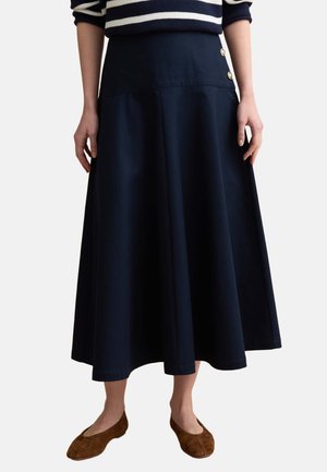 Mujer con falda midi línea A azul marino con botones laterales, combinada con un suéter de rayas y zapatos planos marrones, posando frente a un fondo liso.