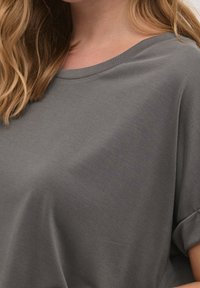 Grå t-shirt med kort ärm som har en bred, rund halsringning och mjukt, texturerat tyg, med en lös design för komfort.