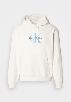 Hanorac de culoare crem, cu buzunar frontale, glugă cu șnur și logo-ul albastru Calvin Klein imprimat pe piept. Material moale din bumbac.