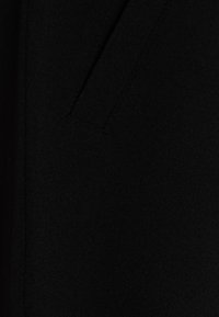 Svart tyg med en slät textur, med en sidoficka och subtila sömnadsdetaljer som framhäver dess skräddarsydda design.