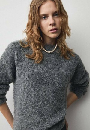 Grijze wollen trui met een gestructureerde afwerking, voorzien van een ronde halslijn en lange mouwen. Gecombineerd met een enkele parelketting.