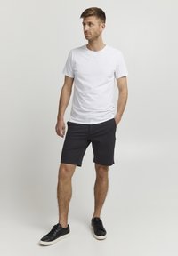 T-shirt en coton blanc, shorts noirs en tissu doux et baskets noires avec une semelle blanche. Design simple et coupe ajustée.