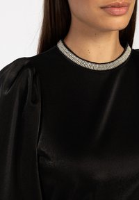 Zwarte satijnen blouse met opbollende mouwen en een glinsterende kraag versierd met kristallen, die een gladde textuur en een elegante uitstraling tentoonstelt.