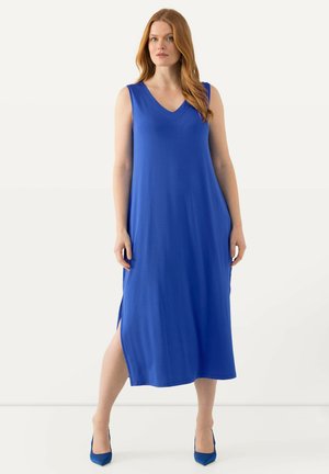 Abito lungo senza maniche di colore blu con scollatura a V, fessure laterali e una consistenza liscia e fluida; indossato con scarpe con tacco blu coordinate.
