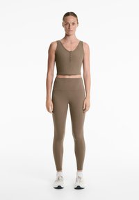 Barna bordázott crop top, gombos kivágással, magas derékú barna leggingsszel párosítva. Mindkét ruha testhez álló és sima tapintású.