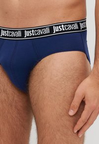 Granatowe slipy z czarnym elastycznym pasem, na którym powtarza się napis „Justcavalli”. Gładki materiał, dopasowany krój i detaliczne szwy.