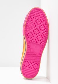 Rosa Gummisohle von Sneakern mit einem geometrischen Profil, das gelbe und lila Akzente an der Seite aufweist, strukturiert für Halt und Langlebigkeit.