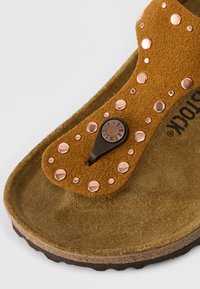 Καφέ σουέτ σανδάλια με χαλκοκολαρίκια και κεντρική ρυθμιζόμενη λωρίδα. Σόλα από φελλό με υφή. Ο λογότυπος της μάρκας ορατός στ η σόλα.