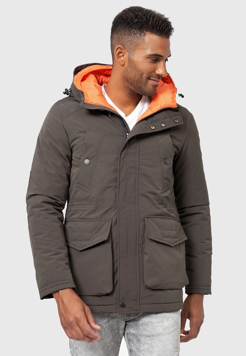 Chaqueta acolchada verde oliva con capucha de color naranja brillante, que cuenta con dos bolsillos frontales y cierre de cremallera. Tela texturizada, diseño aislante.