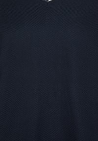 Marinblått stickat tyg med ett strukturerat zigzagmönster, som har en v-ringning och ett mjukt, stretchigt material.