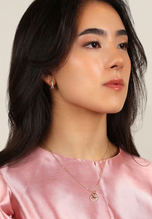 Guld smycken ställda mot en rosa satin topp. Inkluderar hängande örhängen med ett banddesign och ett halsband med en cirkulär medaljong och ädelstenar.