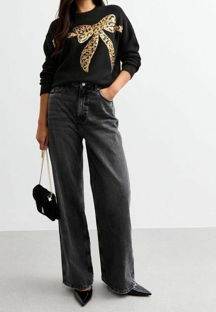 Pull noir avec un nœud doré à imprimé léopard, associé à un jean noir taille haute à jambes larges et des escarpins noirs à bouts pointus. Sac à main noir.