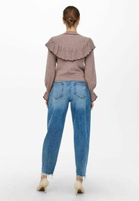 Pull avec col côtelé et dos à volants en mauve. Associé à un jean denim bleu taille haute, avec un ourlet effiloché et des poches arrière.