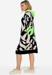 Gevoerd sweatshirt jurkje in zwart en beige met abstracte witte tekst en een neon groene accent. Voorzien van lange mouwen en zijzakken.