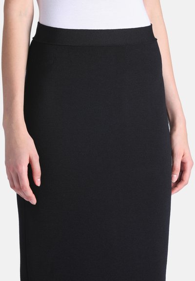 Femme portant une jupe noire cintrée longueur genou avec une taille côtelée et un haut blanc rentré.