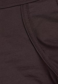 Brunt, elastisk tyg med en slät yta, med synliga sömmar och en subtil glans, utformat för komfort och flexibilitet.