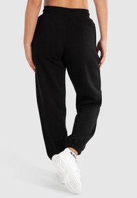 Schwarze Baumwoll-Sweatpants mit elastischem Bund, schmalen Bündchen und Seitentaschen, kombiniert mit weißen Sneakers mit strukturierten Sohlen.