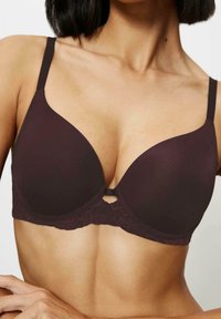 Biustonosz z głęboko burgundowym materiałem, gładkimi miseczkami na drucie i koronkowym detalem na dole. Regulowane ramiączka oraz dekoracyjny zapięcie na środku.