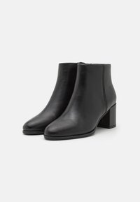 Botines de cuero negro con puntera redondeada, tacón de bloque de altura media y un detalle de costura minimalista en el lateral. Textura suave.