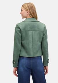Veste en daim vert au design ajusté, avec col et poignets boutonnés ; présente une finition texturée et une silhouette cropped.