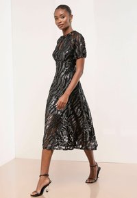 Rochie midi neagră din material transparent cu mărgele, având un model ondulat, mâneci bufante și un corset mulat, completată de o fustă fluidă.