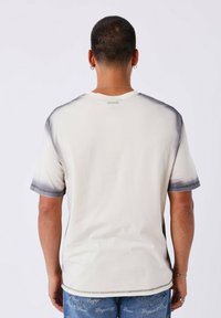 T-shirt a maniche corte color avorio con sfumature grigie sui gomiti. Realizzato in tessuto morbido e liscio, presenta un collo tondo e dettagli di cucitura.