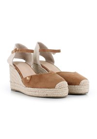 Sandalias de cuña de ante marrón con correas de tela trenzada en los tobillos, punta cerrada y detalles de cuerda de yute en el tacón de cuña. Acento de hardware dorado.