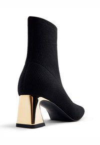 Stivaletto nero realizzato in materiale testurizzato con tacco geometrico dorato, che mette in mostra un design moderno e una silhouette elegante.