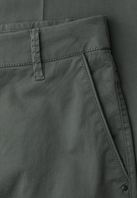 Zbliżenie na szare spodnie materiałowe ukazujące pas, szlufkę na pasek, ukośną kieszeń boczną oraz detale przeszyć.