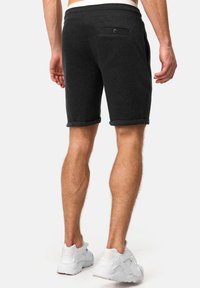 Pantalones cortos de algodón gris oscuro con dobladillo enrollado, que cuentan con un bolsillo trasero con un detalle de botón. Combinados con zapatillas deportivas blancas.