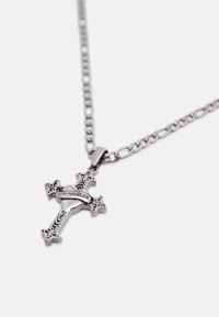 Prívesok z kovu striebornej farby v tvare kríža s ozdobnými detailmi a srdcovým tvarom v strede, na ktorom je vyrytý nápis "LOS ANGELES", zavesený na reťazi.