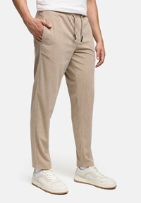 Pantaloni in velluto a coste beige con vita con coulisse, tasche laterali e una texture liscia. Abbinati a sneaker bianche per un look casual.