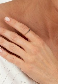 Guld ring med små svarta ädelstenar i rad, som bärs på ett smalt finger. Slät textur och enkel design.