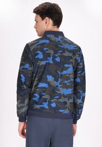 Giubbotto bomber camouflage in navy, grigio e blu. Presenta un colletto e polsini a coste, con una finitura in tessuto liscio e leggero.