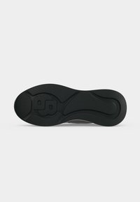 Semelle de chaussure noire avec des motifs en rainures et une lettre B stylisée en relief près du talon, présentée sur un fond clair uni.