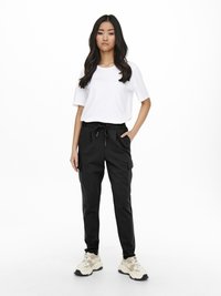 Svarte cargo bukser med sidelommer, parret med en ensfarvet hvid t-shirt. Model iført lys beige sneakers. Minimalistisk design, afslappet pasform.