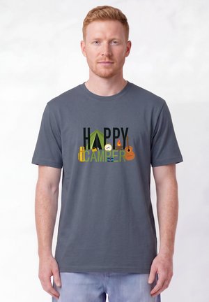 Homme roux portant un t-shirt gris avec le texte "Happy Camper" et des icônes de camping comprenant tente, boussole, lanterne, feu de camp et guitare.