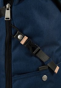 Sac à dos bleu marine en tissu texturé, avec une fermeture éclair noire, des accents en cuir, une sangle ajustable et des détails en métal.