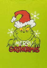 Maglietta verde con un Grinch in stile cartoon che indossa un cappello di Babbo Natale rosso e bianco, con la scritta "BUON GRINCHMAS" e disegni di fiocchi di neve.