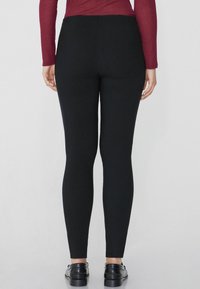 Leggings noirs au design ajusté, texture lisse et taille haute, associés à des chaussures noires à enfiler. Vue arrière affichée.