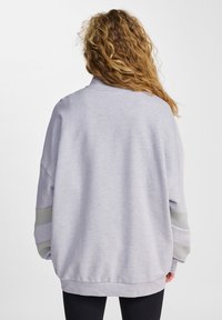 Ljusgrå sweatshirt med en löst sittande passform, rund nacke och långa ärmar som har gröna ränder på ärmarna och en ribbad nederkant.