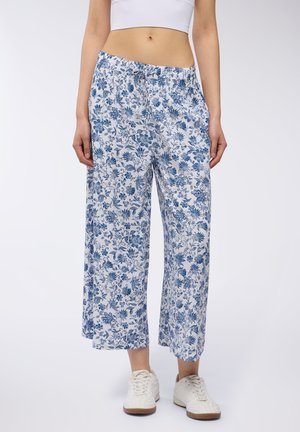 Pantaloni bianchi a gamba larga con un motivo floreale blu, cintura elastica e cordoncino. Abbinati a sneakers bianche per un look casual.